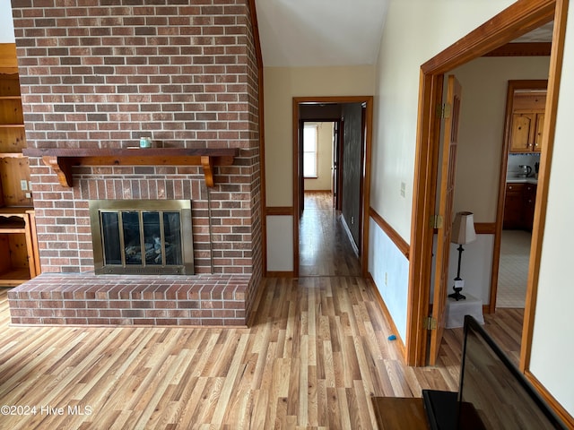 unfurnished living room featuring light hardwood / wood-style floors, lofted ceiling, and a brick fireplace