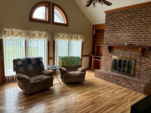 living room featuring ceiling fan, wood-type flooring, high vaulted ceiling, and a brick fireplace