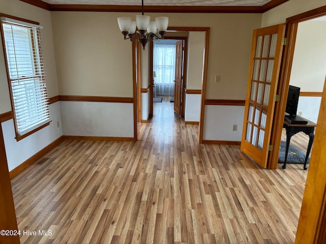 empty room featuring ornamental molding, light wood-type flooring, french doors, and a notable chandelier