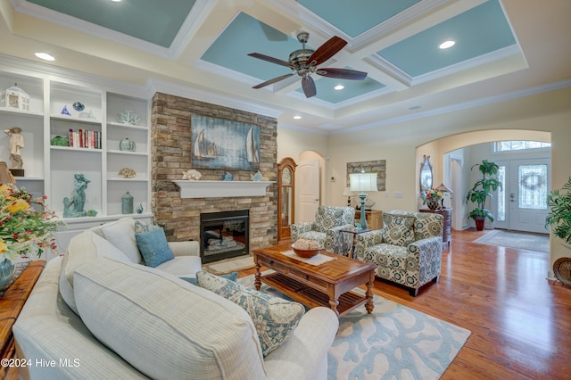 living room with coffered ceiling, a stone fireplace, crown molding, hardwood / wood-style flooring, and ceiling fan