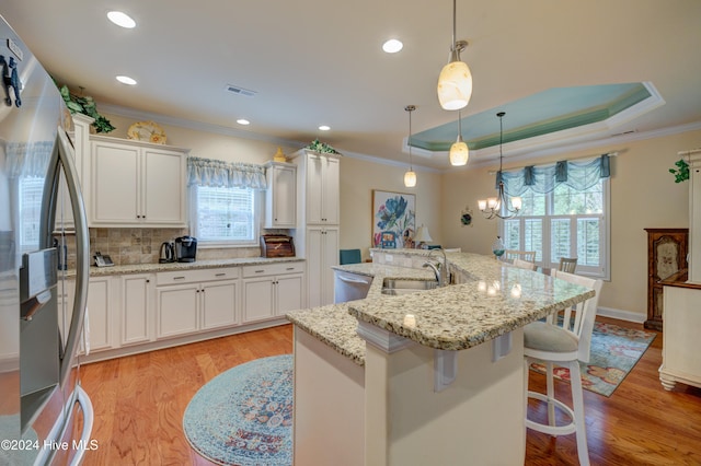 kitchen with pendant lighting, a kitchen island with sink, white cabinets, light wood-type flooring, and appliances with stainless steel finishes