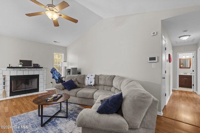 living room featuring hardwood / wood-style floors, ceiling fan, lofted ceiling, and a tile fireplace