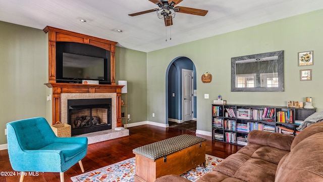 living room with ceiling fan, a large fireplace, and dark wood-type flooring