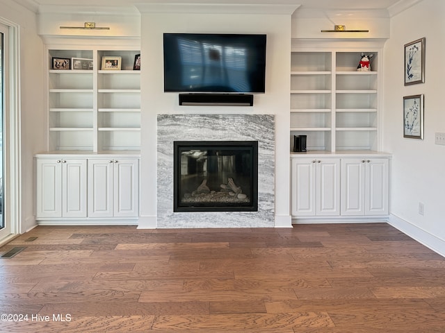 unfurnished living room featuring a premium fireplace, hardwood / wood-style floors, crown molding, and built in features