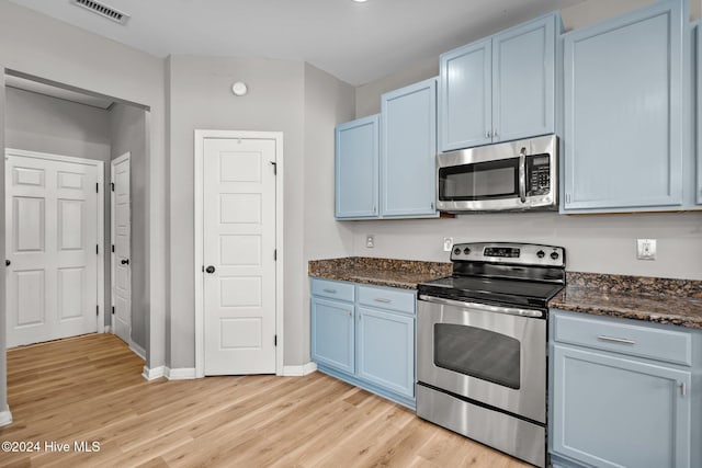 kitchen featuring dark stone counters, blue cabinetry, appliances with stainless steel finishes, and light hardwood / wood-style flooring