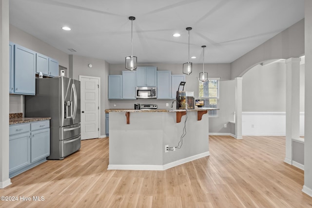 kitchen with appliances with stainless steel finishes, light wood-type flooring, hanging light fixtures, and a breakfast bar area