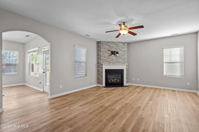 unfurnished living room featuring ceiling fan, light wood-type flooring, a fireplace, and a wealth of natural light