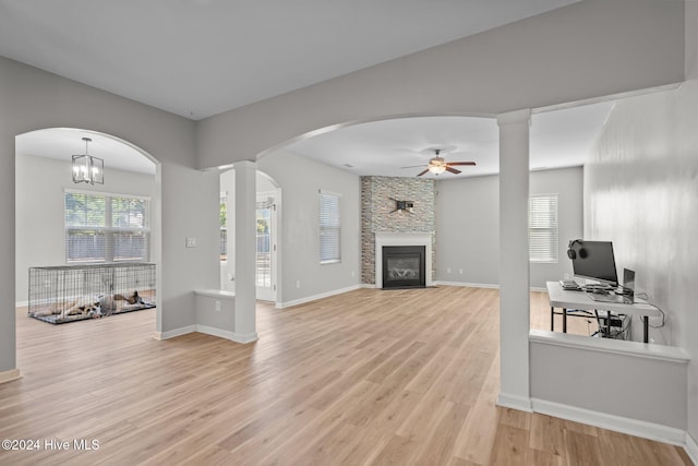 living room featuring ceiling fan with notable chandelier, light hardwood / wood-style floors, and a stone fireplace