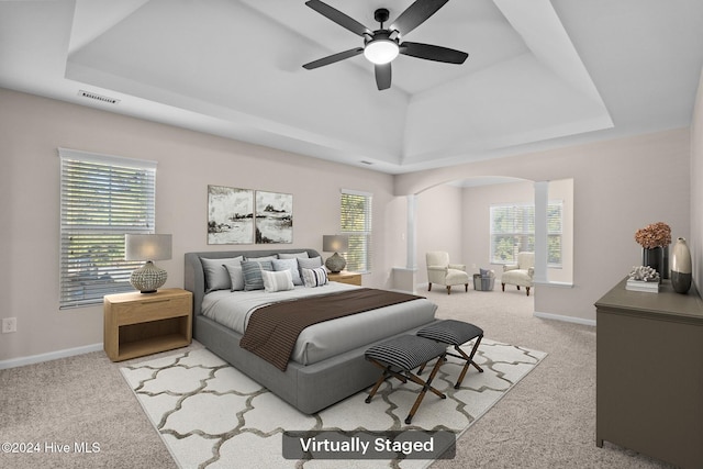 carpeted bedroom with ceiling fan, a tray ceiling, and multiple windows