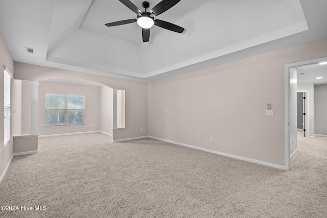 empty room featuring a raised ceiling, ceiling fan, and light colored carpet