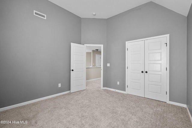 unfurnished bedroom with light carpet, a closet, and high vaulted ceiling