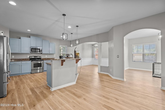 kitchen with sink, stainless steel appliances, decorative light fixtures, a breakfast bar area, and light wood-type flooring