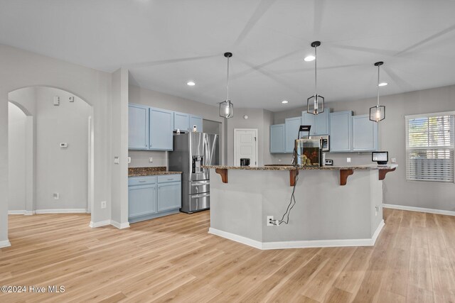 kitchen with stainless steel fridge with ice dispenser, light wood-type flooring, a center island with sink, and a breakfast bar area