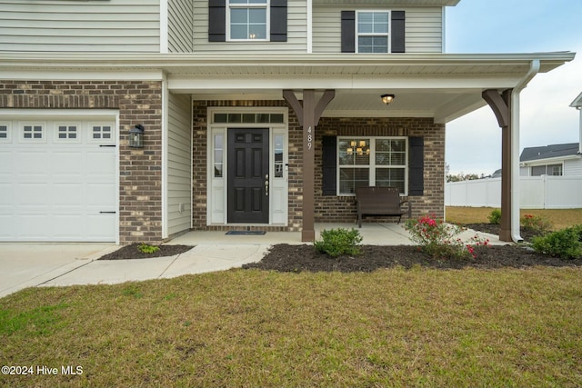 view of exterior entry with covered porch, a yard, and brick siding