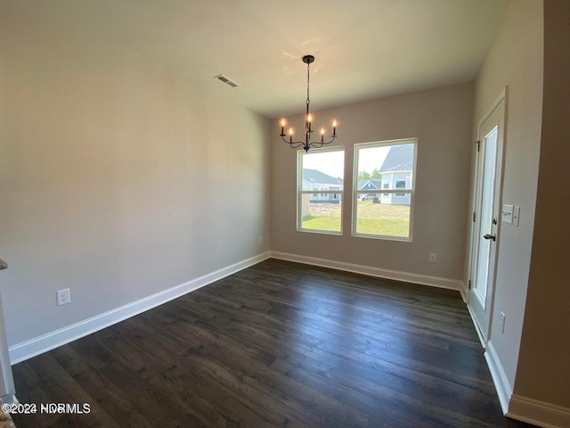 spare room with dark hardwood / wood-style flooring and an inviting chandelier