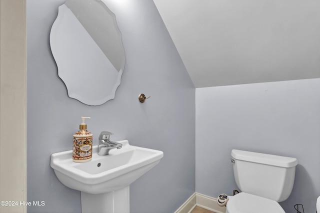 bathroom featuring toilet, sink, and vaulted ceiling