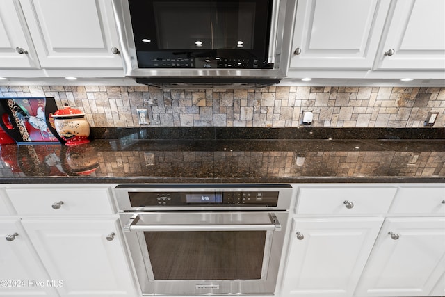 kitchen featuring appliances with stainless steel finishes, tasteful backsplash, white cabinetry, and dark stone countertops