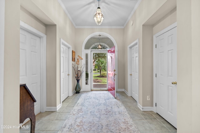 tiled foyer entrance featuring crown molding and an inviting chandelier