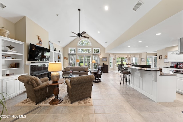 living room with light tile patterned floors, ceiling fan with notable chandelier, and high vaulted ceiling