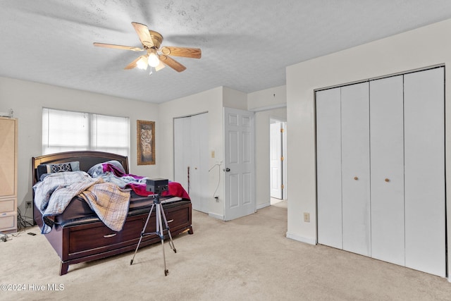 carpeted bedroom with ceiling fan, a textured ceiling, and two closets