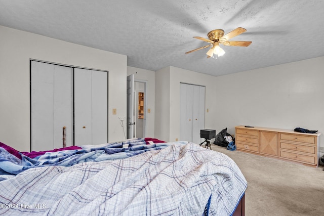 bedroom with ceiling fan, light colored carpet, a textured ceiling, and two closets