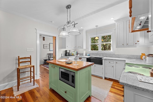 kitchen with stainless steel microwave, light wood-type flooring, butcher block countertops, a kitchen island, and white cabinetry