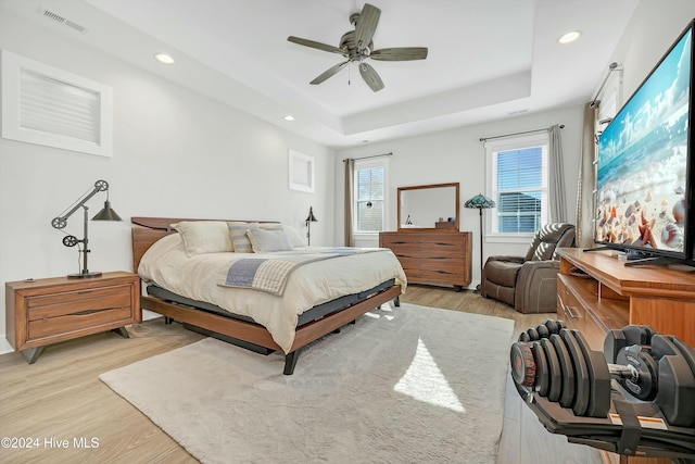 bedroom with light hardwood / wood-style floors, a raised ceiling, and ceiling fan