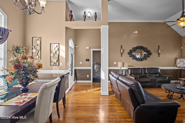 living room with ceiling fan with notable chandelier, light hardwood / wood-style floors, crown molding, and high vaulted ceiling