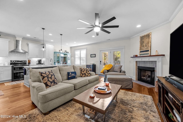 living room with ceiling fan, crown molding, sink, light hardwood / wood-style flooring, and a tiled fireplace