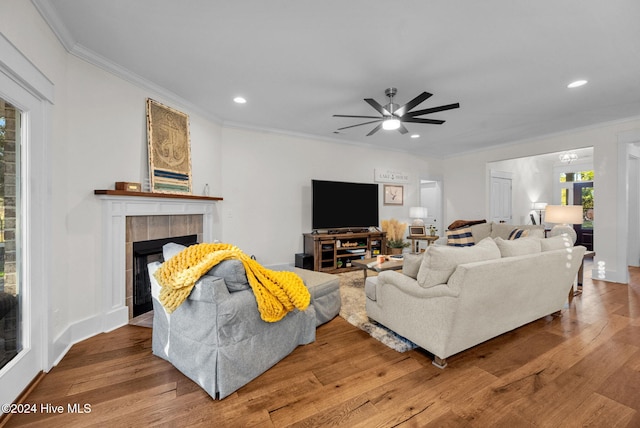 living room featuring a tiled fireplace, crown molding, ceiling fan, and hardwood / wood-style flooring