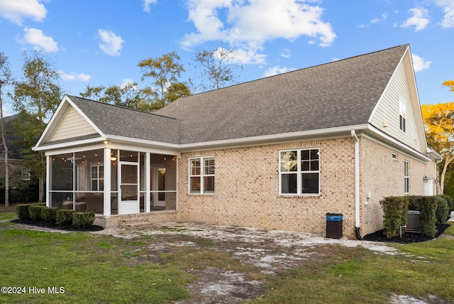 back of house featuring a yard, a shingled roof, brick siding, and a sunroom