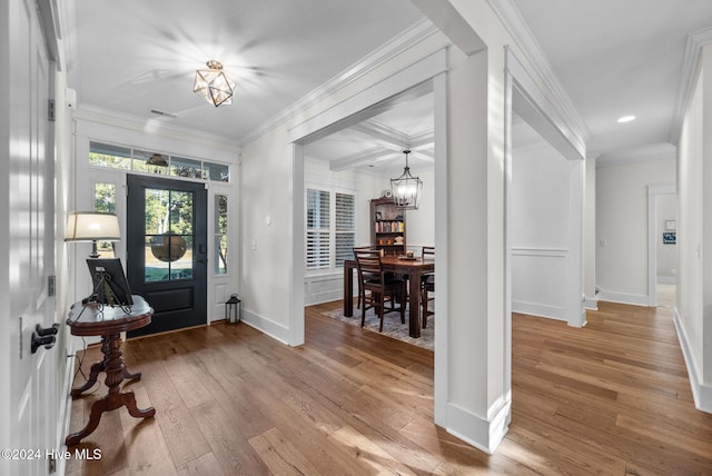 foyer with beamed ceiling, wood-type flooring, ornamental molding, and a chandelier