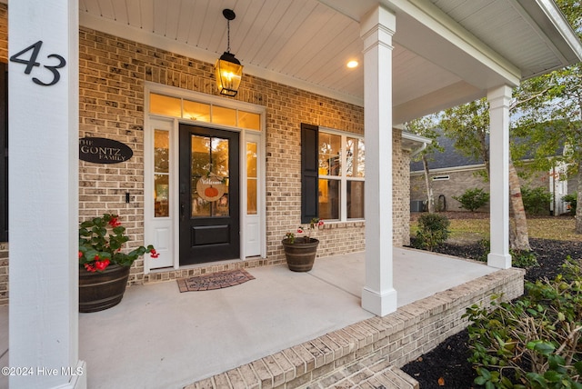 entrance to property featuring a porch and brick siding