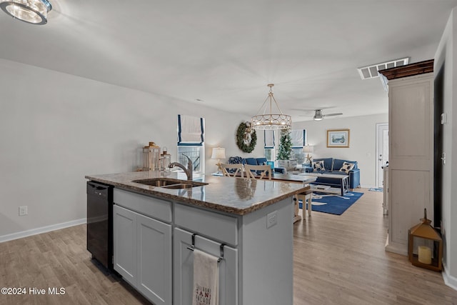 kitchen with light stone countertops, light wood-type flooring, ceiling fan, a center island with sink, and black dishwasher