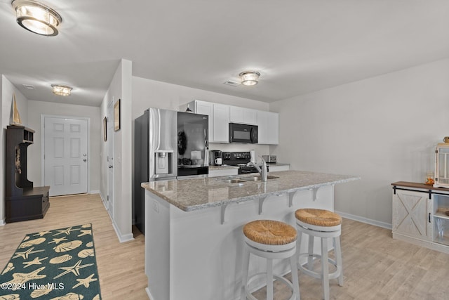 kitchen with black appliances, white cabinets, sink, light stone countertops, and light hardwood / wood-style floors