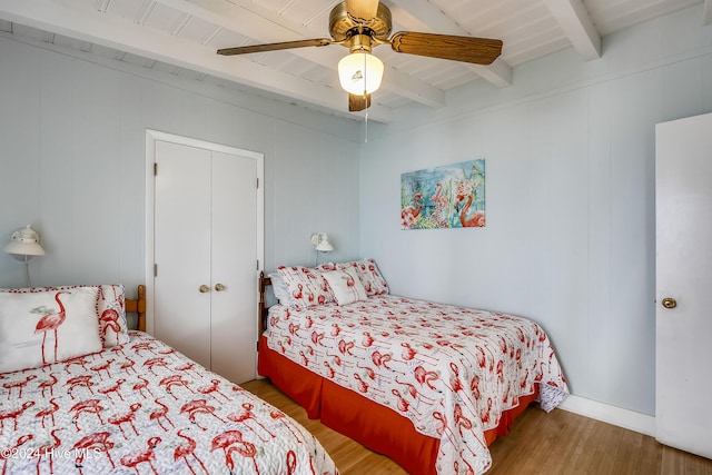 bedroom featuring beam ceiling, ceiling fan, wood walls, wood-type flooring, and a closet