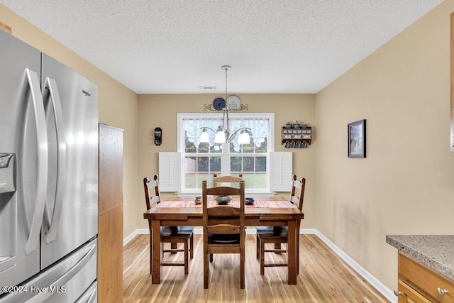 dining space with light hardwood / wood-style floors, a textured ceiling, and a notable chandelier