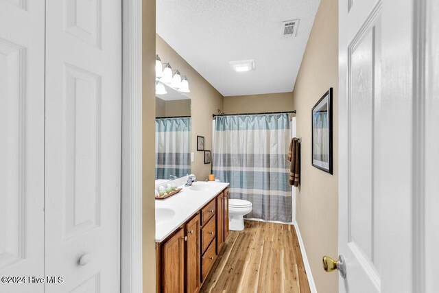 bathroom featuring toilet, a textured ceiling, hardwood / wood-style flooring, walk in shower, and vanity