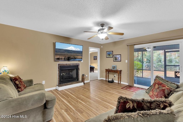 living area featuring light wood-style floors, baseboards, a fireplace with raised hearth, and a textured ceiling