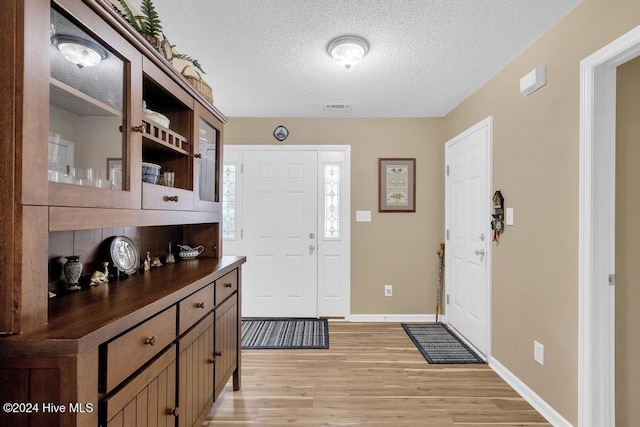 entryway with light wood-type flooring and a textured ceiling