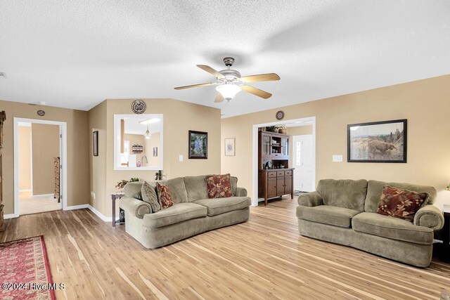 living room featuring light wood-type flooring, ceiling fan, and a textured ceiling