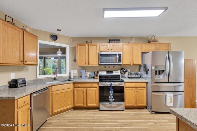 kitchen featuring pendant lighting, stainless steel appliances, light hardwood / wood-style floors, sink, and light brown cabinetry