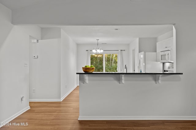 kitchen featuring a breakfast bar, dark countertops, light wood-style flooring, a chandelier, and white appliances