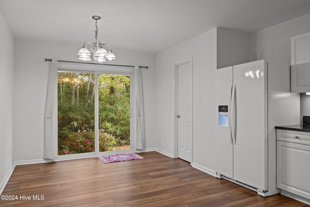 unfurnished dining area featuring baseboards, dark wood finished floors, and an inviting chandelier