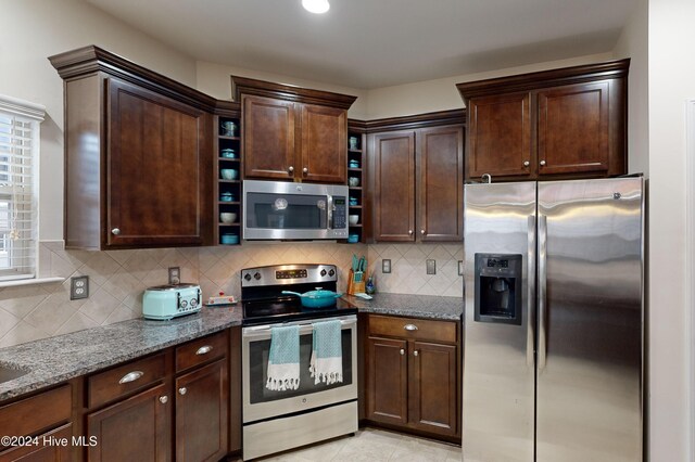 kitchen featuring dark stone countertops, light tile patterned floors, tasteful backsplash, dark brown cabinets, and stainless steel appliances