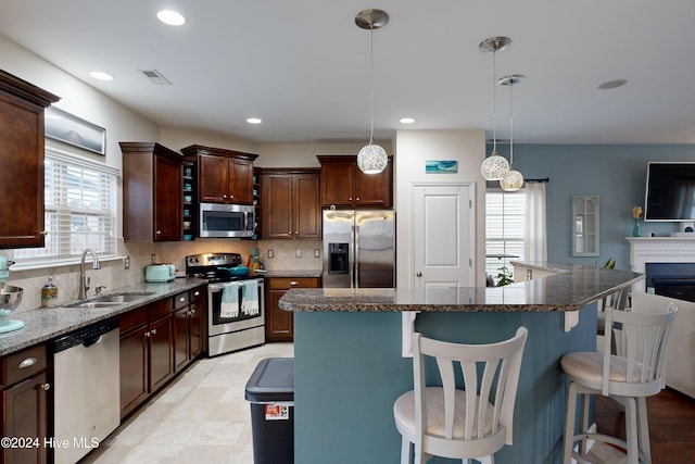 kitchen featuring appliances with stainless steel finishes, a center island, decorative light fixtures, and sink