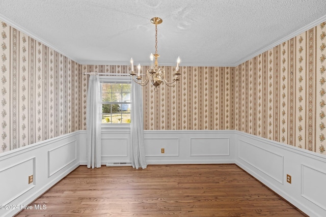 unfurnished dining area featuring ornamental molding, wood-type flooring, and an inviting chandelier