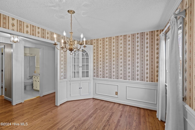 unfurnished dining area with hardwood / wood-style floors, ornamental molding, a textured ceiling, and a chandelier