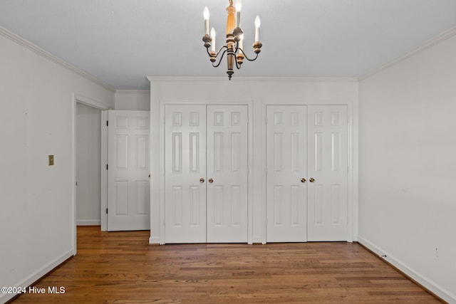 unfurnished bedroom with a chandelier, wood-type flooring, crown molding, and two closets