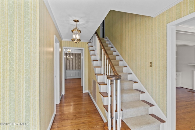 staircase featuring wood-type flooring, crown molding, and an inviting chandelier